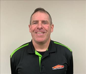 Man with short hair smiling for employee photo with black and green Servpro polo on. 